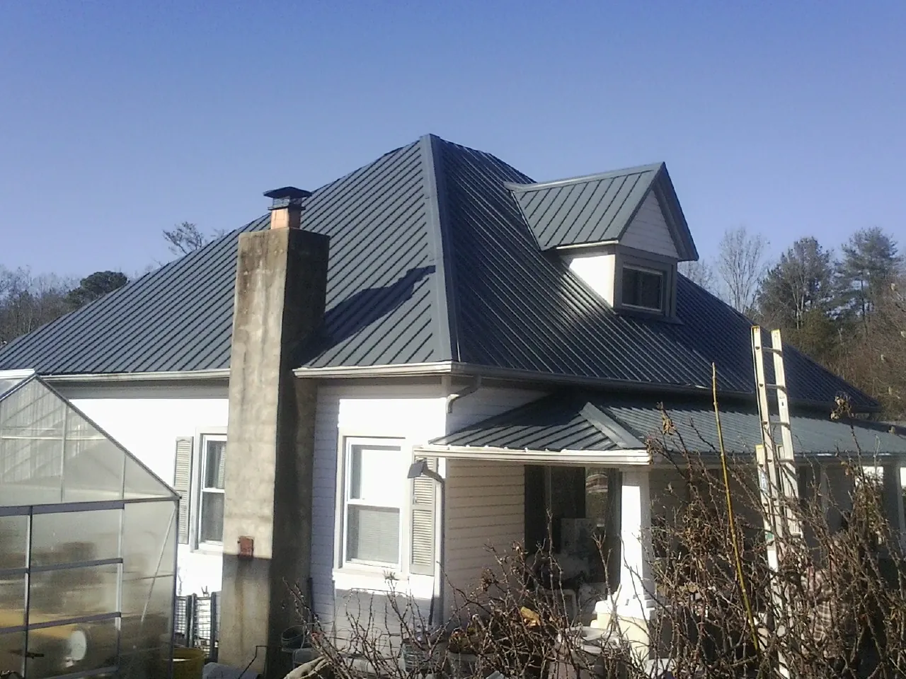 Dark blue standing seam metal roof on a white farmhouse with dormer — Slate & Tile Roof Repair by Roofing Brothers in La Puente