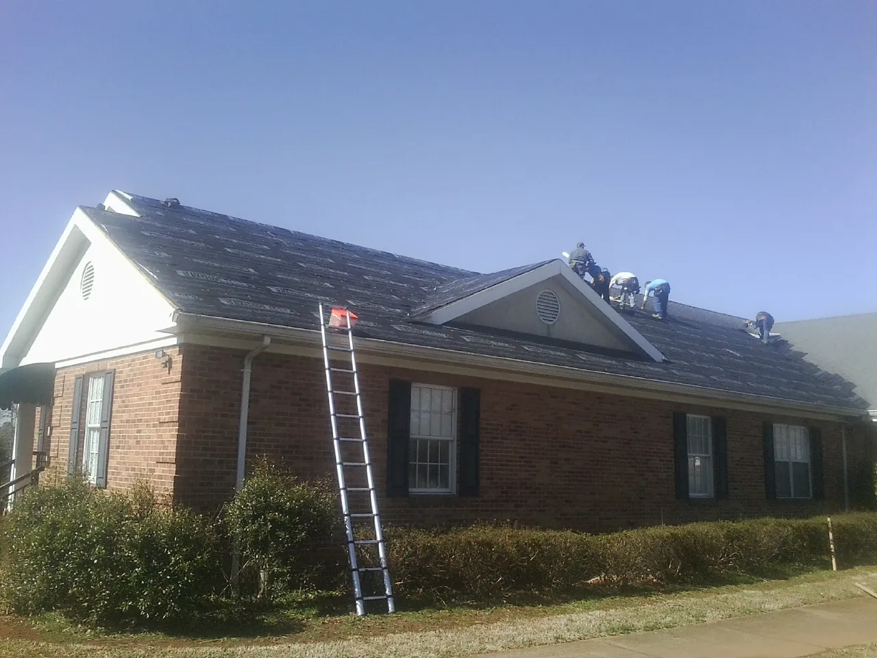 Crew tearing shingles off a brick ranch roof with a ladder set — Emergency Roof Repair work by our crew in La Puente