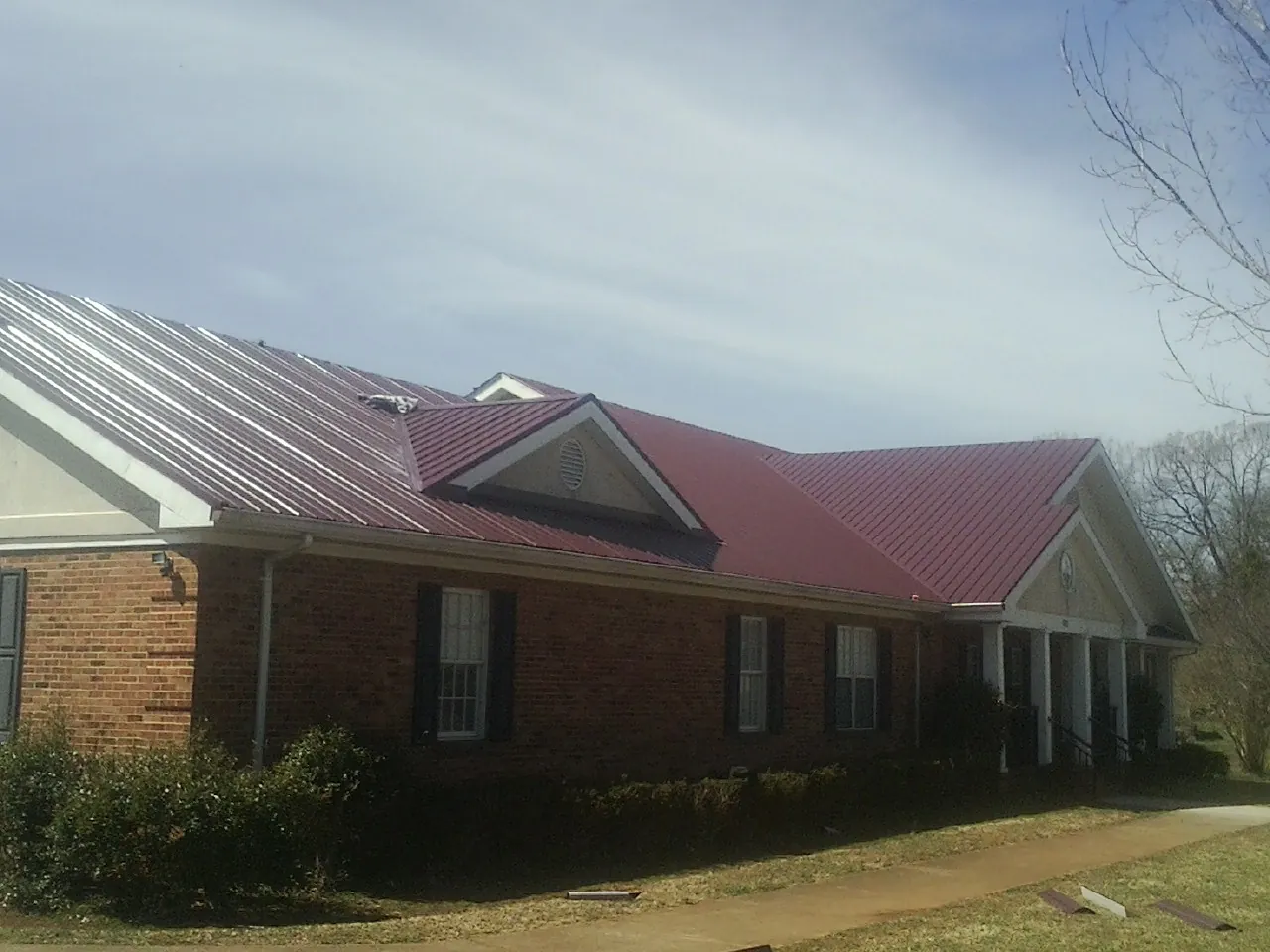 Red metal roof with gabled entries on a long brick building, from a Hail Damage Roof Repair job in La Puente