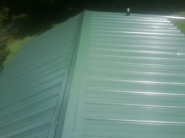 New green metal panels meeting at the ridge of a roof — Flat Roof Repair work by our crew in La Puente