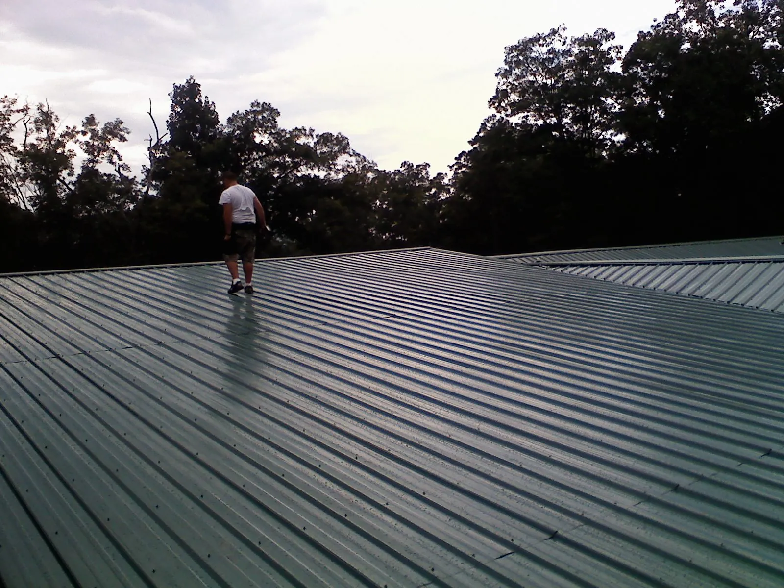 Roofer walking a wide expanse of new green metal roofing in La Puente