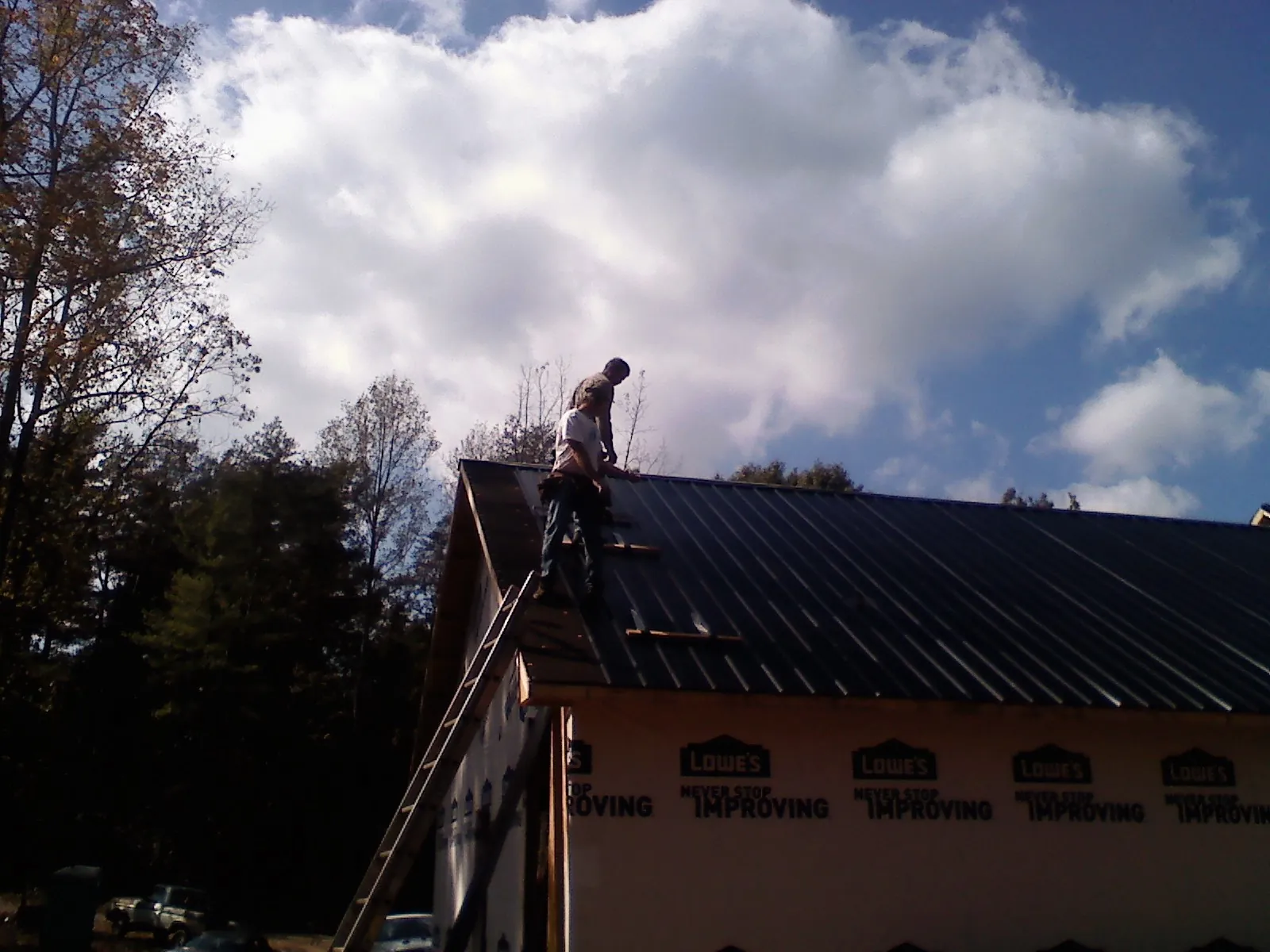 Roofer fastening dark metal panels high against a cloudy sky, from a Roof Inspection job in La Puente