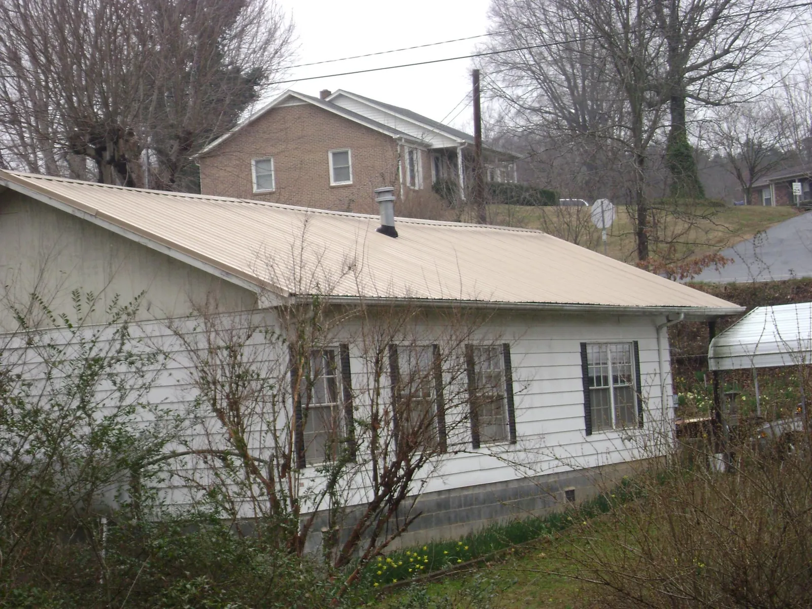 Tan metal roof on a white sided house set into a hillside — Commercial Roofing by Roofing Brothers in La Puente